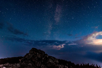 Milky Way galaxy in the night sky above rocky mountain and stormy clouds