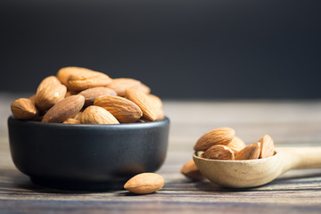 Almonds in black bowl (roasted) on wooden background