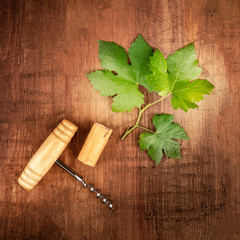 A vine leaf with a vintage corkscrew and a cork, overhead square shot on an oak barrel