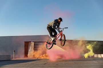 BMX rider on a rooftop jumping and using smoke grenades