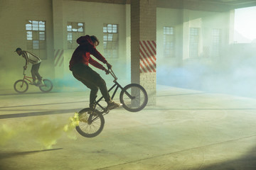 BMX riders in an empty warehouse using smoke grenades