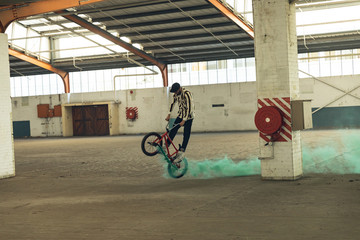 BMX rider in an empty warehouse using smoke grenade