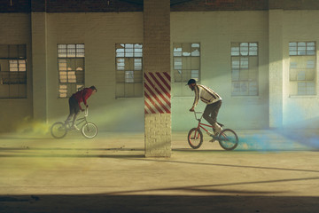 BMX riders in an empty warehouse using smoke grenades