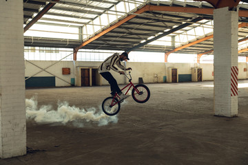 BMX rider in an empty warehouse using smoke grenade