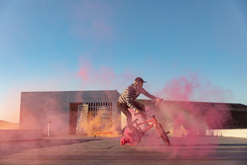BMX rider on a rooftop using smoke grenades