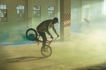 BMX riders in an empty warehouse using smoke grenades