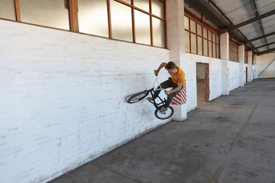 BMX rider in an empty warehouse riding on wall - Powered by Adobe
