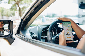 Close-up of female hand holding mobile phone with car sharing app while driving a car