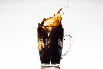 Splash on transparent coffee cup on dark reflective table with spilled coffee.