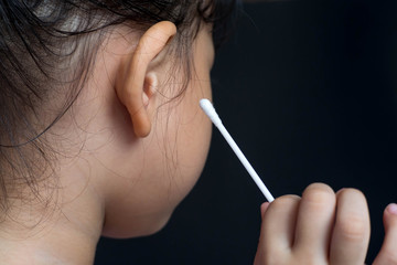 Asian girl use cotton bud to clean her ear by herself.Cleaning child ear concept
