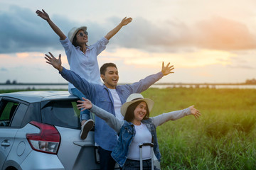  Relax in the jungle.Young Asian three people sitting on the roof hatchback. Along with two hands in the air.Three Friends glad to travel to their destination by car.