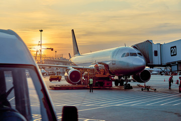 Modern passenger airplane parked to terminal building gate at airside apron of airport with close...