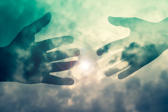 surreal image of hands silhouette with glow of light in blue color gradient cloudy sky,concept image