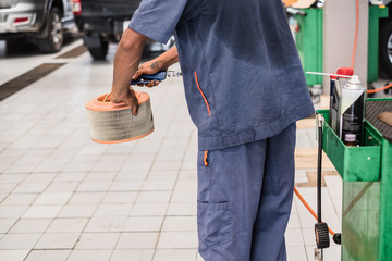 Auto mechanic using the blower to clean the car air filter.