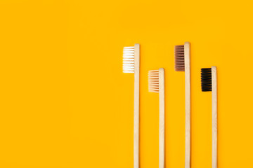 Four eco-friendly bamboo toothbrushes on a hot yellow background. Copy space. Zero waste concept, plastic-free, organic, eco-friendly shopping