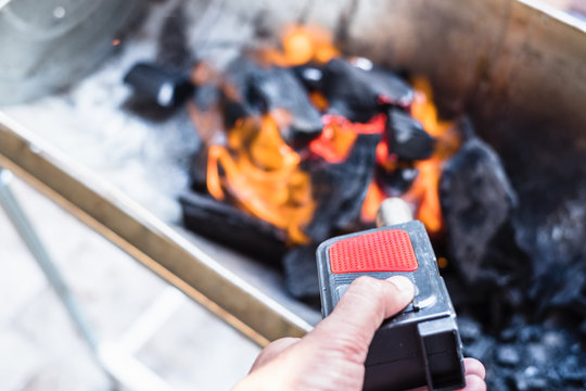 Close up of man's hand holding and using air fire blower to set stove charcoal fire.