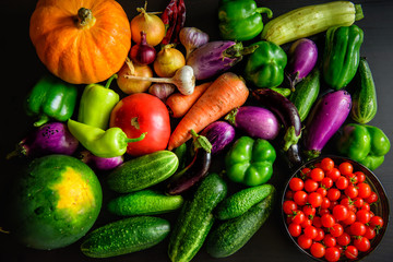 Harvest or Thanksgiving background with autumn vegetables on dark table. Seasonal ingredients for cooking: pumpkin, onions, carrots, eggplant, tomatoes, paprika, garlic, cucumbers. Top view, close-up.