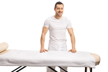 Professional young masseur posing behind a massage bed - obrazy, fototapety, plakaty
