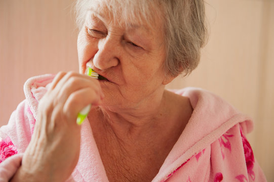 Elderly grandmother in pink terry bathrobe brushes her teeth in bathroom. Hygienic procedures. Pensioners in sanatorium