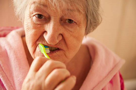 Elderly grandmother in pink terry bathrobe brushes her teeth in bathroom. Hygienic procedures. Pensioners in sanatorium