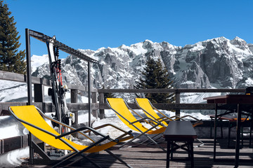 View of the cafe outdoor terrace on the ski slope with orange loungers on it.