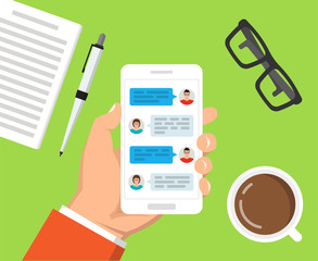 Hand holding smartphone with text messaging on the screen. Сup of coffee, notebook with pen and glasses lay on the table. Vector flat illustration.
