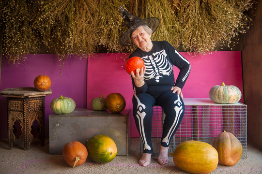 An elderly witch grandmother is sitting in a barn. old woman dressed in skelton costumes. Halloween eve with pumpkins in hands