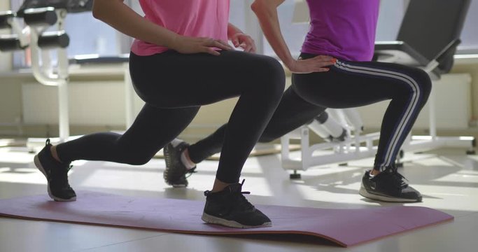 Young woman and instructor do low lunge in gym