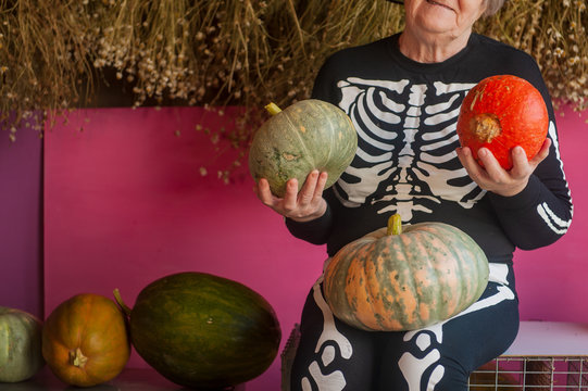 An elderly witch grandmother is sitting in a barn. old woman dressed in skelton costumes. Halloween eve with pumpkins in hands