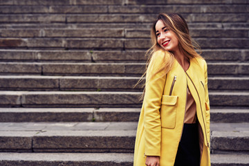 Portrait of a young beautiful laughing woman with long hair  and a yellow jacket on a cloudy day. Close-up.