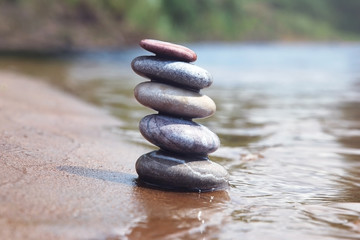 Stack of balancing pebble stones on sand and water edge. Zen symbol against blurred nature background.