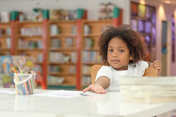 Little toddler girl mixed Asian and Africcan sitting in the library looking at the camera.