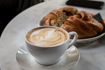 Full cup of cappuccino and pastry on table