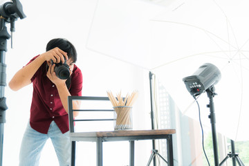 young man photographer in a red shirt is working to take pictures in the studio with a digital camera lighting and spotlight equipment