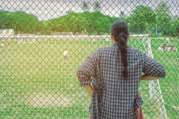 Back view of female parent cheering children playing football in school.