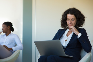 Positive confident business leader working on computer in office lounge. Business woman sitting in...