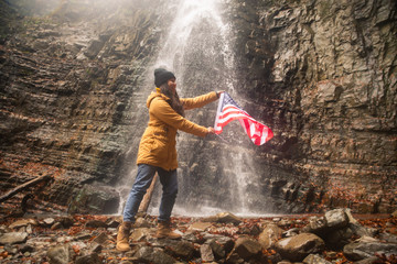 young caucasian adult female with usa flag in front of waterfall