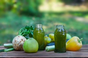 Healthy green smoothie with apples, grapes, cucumber and celery. Fruit and vegetable juice on wooden table, with blured nature in  background. Outdoor image.