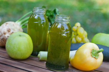 Healthy green smoothie with apples, grapes, cucumber and celery. Fruit and vegetable juice in little bottles on wooden table, with blured nature in  background.