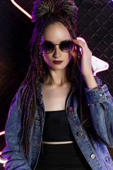 Beautiful girl with a cornrows hairstyle, wearing denim jacket and sunglasses, posing in a night...