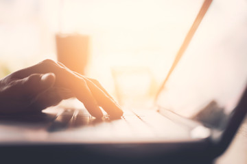 Man hand using keyboard laptop on wood table in coffee shop.