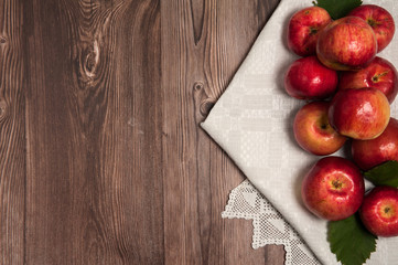 Autumn composition. Red apples, green leaves, linen napkin with handmade lace on a wooden background.