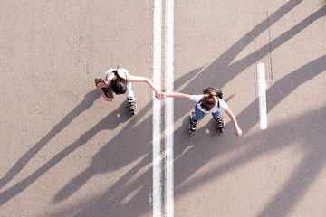 Girls friends rollerblading in city park holding each other hands 