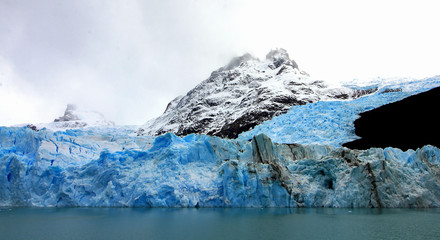 Un viejo glaciar azul con una montaña nevada en el fondo