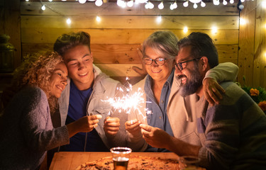 Happy family of four people sparkling wishing a wonderful new year 2020. Large pizza on the wooden table. Multi generation. Concept of happiness and love