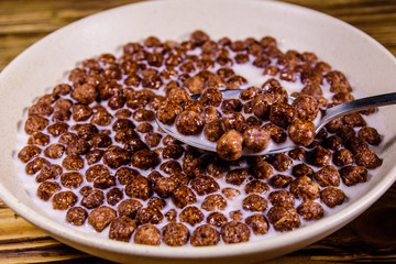 Ceramic plate with chocolate cereal balls in milk on wooden table