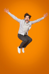 Crazy man jumping with raised arms over orange background