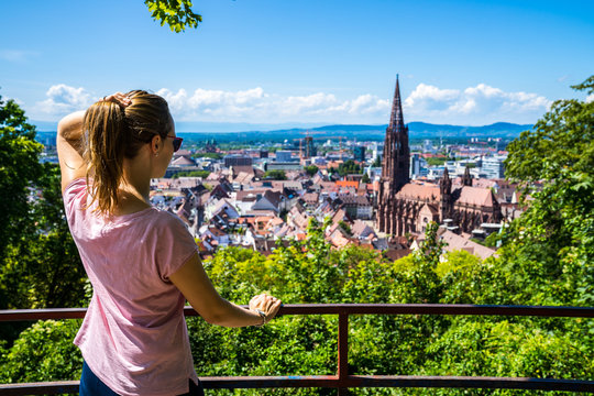 Germany, Stunning young woman standing above cityscape of freiburg im breisgau old town and famous minster cathedral in summertime
