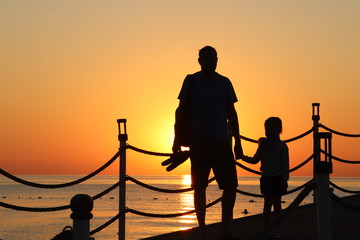 Fototapeta na wymiar Black silhouettes of an adult and child at sunset or people look at the beautiful sea sunset.