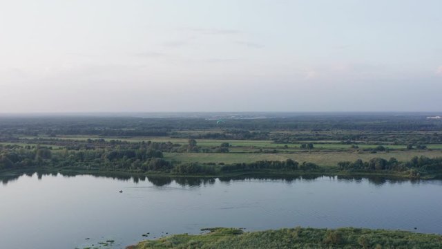 Aerial landscape green fields and forests on river shore. Drone view parasail flying over river water on skyline background. Parasailing on golden sunset in sky background